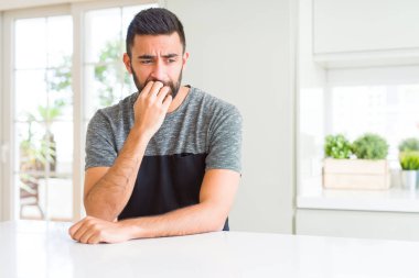 Yakışıklı İspanyol adam evde rahat t-shirt giyen stresli ve sinirli ağız tırnakısırma elleri ile bakıyor. Anksiyete sorunu.