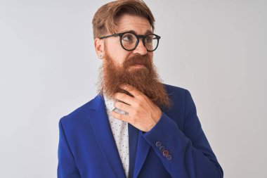 Genç kızıl İrlandalı işadamı takım elbise ve gözlük giyen izole beyaz arka plan üzerinde el çene soru, dalgın ifade düşünme. Düşünceli bir yüzle gülümsüyor. Şüphe kavramı.