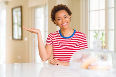 Gülümseyen genç güzel Afrikalı-Amerikalı kadın evde neşeli sunulması ve kameraya bakarak avucunun ile işaret.