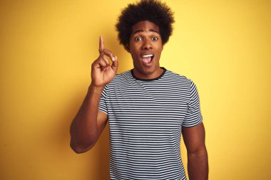 Afro saçlı Afro-Amerikalı adam izole sarı arka plan üzerinde lacivert çizgili t-shirt giyen başarılı bir fikir ile parmak işaret. Çıktı ve mutlu. Bir numara.