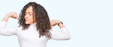 Kıvırcık saç ile genç güzel kadın kazak gülen silah kasları gösteren balıkçı yaka kazağı giyiyor. Fitness konsepti.