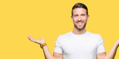 Casual beyaz t-shirt gülen iki elle gösterilen giyen yakışıklı adam açık avuç içi, sunmak ve reklam karşılaştırma ve denge