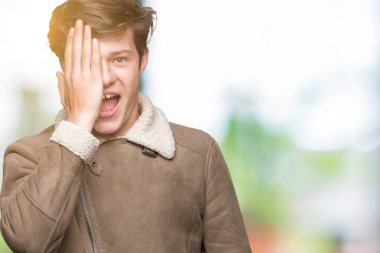 El yüz ve sürpriz duygu kendinden emin gülümseme ile tek gözüyle kapsayan izole arka plan üzerinde kış ceket giyen genç yakışıklı adam.