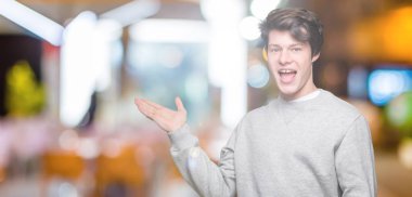 Neşeli sunulması ve kameraya bakarak avucunun ile işaret gülümseyen izole arka plan üzerinde sweatshirt giyen genç yakışıklı sportif adam.