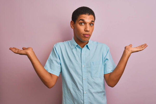 Молодой красивый арабский мужчина в голубой рубашке стоял на изолированном розовом фоне, ничего не зная и смущенное выражение лица с поднятыми руками и руками. Концепция сомнений
.