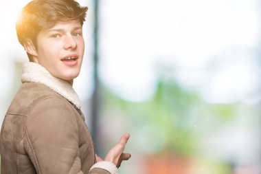 Açık el ile doğal gülümseyen girmek için izole arka plan davet üzerine kış ceket giyen genç yakışıklı adam