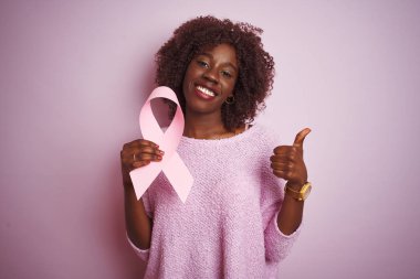 Genç afrikalı afro kadın izole pembe arka plan üzerinde ayakta tutan büyük bir gülümseme ok işareti yapıyor mutlu, parmakları ile başparmak, mükemmel işareti