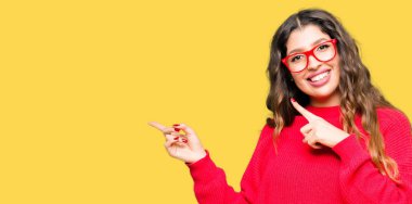 Gülümseyen ve iki elleri ve parmakları ile tarafına işaret kamera bakarak kırmızı gözlük takan genç güzel kadın.