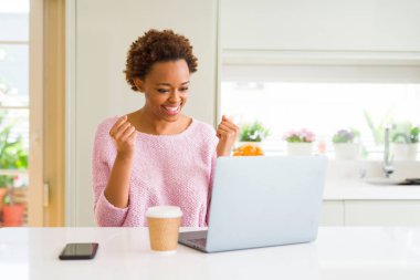 Bilgisayar lı dizüstü bilgisayar kullanarak çalışan genç Afro-Amerikan kadın, kollarını kaldırıp gözleri açık bir şekilde başarıya uğrup büyülemesine neden oldu. Kazanan kavramı.