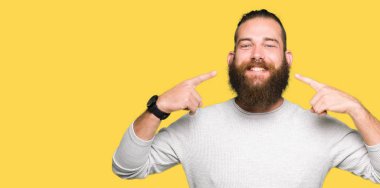 Genç sarışın adam rahat kazak giyen emin gösteren gülümseyerek ve parmakları diş ve ağız ile işaret. Sağlık kavramı.