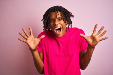 Afro amerikan adam dreadlocks giyen t-shirt izole pembe arka plan üzerinde deli kutluyor ve silah kaldırdı ve açık gözleri ile başarı için hayran heyecanlı çığlık. Kazanan kavramı