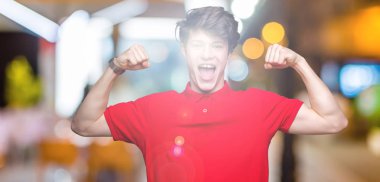 Kol kasları gururlu gülümseyen gösterilen izole arka plan üzerinde kırmızı t-shirt giyen genç yakışıklı adam. Fitness kavramı.