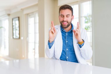 Klinikte tıbbi palto giyen yakışıklı doktor umut la parmaklarını keserek gülümseyerek gözleri kapalı. Şans ve batıl kavram.