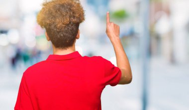 Kırmızı t-shirt giyen afro saçlı genç yakışıklı adam parmak eliyle arkadan işaret eden geriye doğru poz