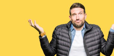 Kış ceket clueless ve şaşkın bir ifadeyle kollar ve eller kaldırdı giyen yakışıklı adam. Şüphe kavramı.