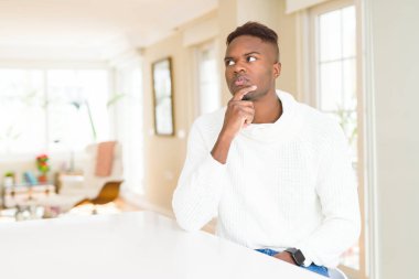 Çene düşünme hakkında soru, dalgın ifade üzerine el ile yakışıklı Afrikalı-Amerikalı adam beyaz masada. Düşünceli yüzüyle gülümsüyor. Şüphe kavramı.