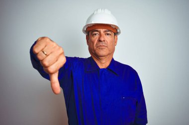 Izole beyaz arka plan üzerinde üniforma ve kask giyen Yakışıklı orta yaş işçi adam mutsuz ve kızgın gösteren reddi gösteren ve aşağı jest başparmak ile negatif. Kötü ifade.
