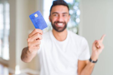 Yakışıklı İspanyol adam tutan kredi kartı çok mutlu yan el ve parmak ile işaret