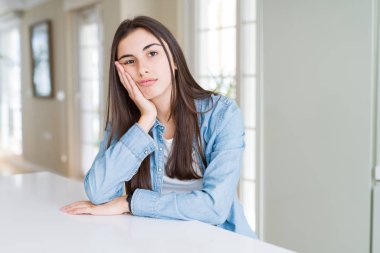 Güzel genç kadın evde beyaz masada oturan yorgun görünümlü ve çapraz kolları ile depresyon sorunları ile sıkılmış düşünme.