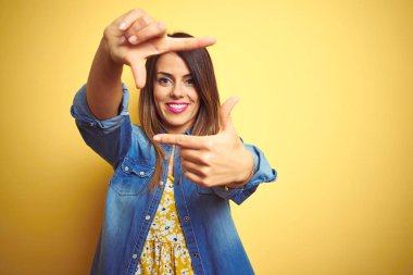 Genç güzel kadın mutlu yüz ile elleri ve parmakları ile çerçeve yapma sarı izole arka plan üzerinde duran gülümseyerek. Yaratıcılık ve fotoğrafçılık konsepti.