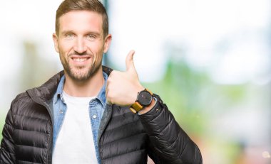 El ile jest kadar mutlu thumbs yapıyor kış ceket giyen yakışıklı adam. Başarı gösteren kameraya bakarak ifadeyi onaylama.