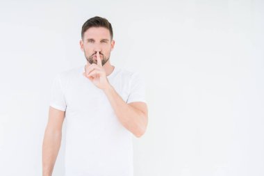 Dudaklarında parmak ile sessiz olmanı izole arka plan üzerinde rahat beyaz t-shirt giyen genç yakışıklı adam. Sessizlik ve gizli kavramı.