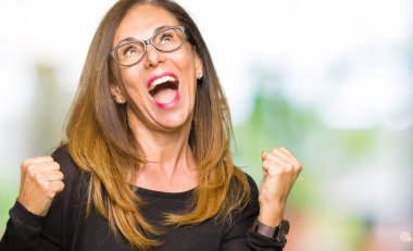 Gülümseyen ve başarı için çığlık çok mutlu ve heyecanlı kaldırdı, silah ile kazanan jest yapıyor gözlüklü güzel orta yaş kadın. Kutlama kavramı.