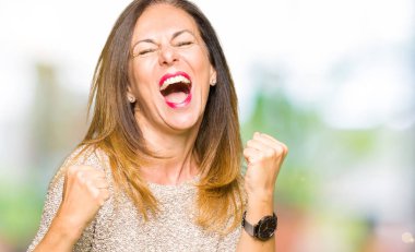 Moda kazak giyen güzel orta yaş kadın çok mutlu ve heyecanlı silah kaldırdı, gülümseyen ve başarı için çığlık ile kazanan jest yapıyor. Kutlama konsepti.