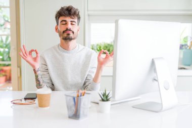 Bilgisayar kullanarak çalışan genç adam rahatlayın ve gözleri kapalı parmakları ile meditasyon jest yapıyor gülümseyerek. Yoga konsepti.