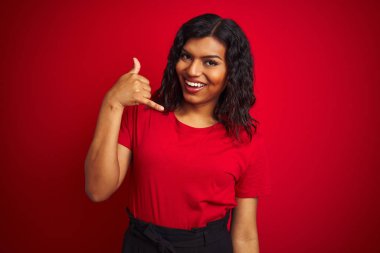 Beautiful transsexual transgender woman wearing t-shirt over isolated red background smiling doing phone gesture with hand and fingers like talking on the telephone. Communicating concepts. clipart