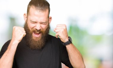 Silah ile başarı için giyiyor rahat t-shirt heyecanlı genç sarışın adam zafer kutluyor gülümseyen kaldırdı. Kazanan kavramı.