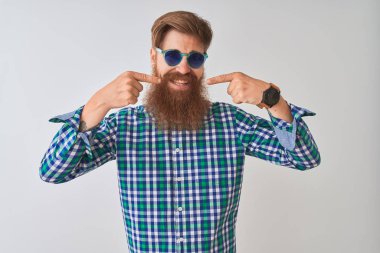Genç kızıl İrlandalı adam izole beyaz arka plan üzerinde rahat gömlek ve güneş gözlüğü giyen neşeli gösteren gülümseyerek ve parmakları diş ve ağız ile işaret. Diş sağlığı kavramı.