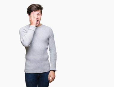 El yüz ve sürpriz duygu kendinden emin gülümseme ile tek gözüyle kapsayan izole arka plan üzerinde kış kazak giyen genç yakışıklı adam.