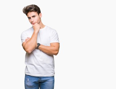 Çene düşünme hakkında soru, dalgın ifade üzerine el ile izole arka plan üzerinde beyaz t-shirt giyen genç yakışıklı adam. Düşünceli yüzüyle gülümsüyor. Şüphe kavramı.