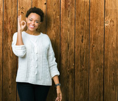 İzole arka plan el ve parmaklar ok işaretiyle yapıyor olumlu gülümseyen üzerinde kazak giyen güzel genç Afro-Amerikan kadın. Başarılı ifade.