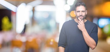 Emin çapraz kollar ve çeneme kaldırdı el ile gülümseme ile kameraya bakarak izole arka plan üzerinde kazak giyen genç yakışıklı adam. Pozitif düşünce.