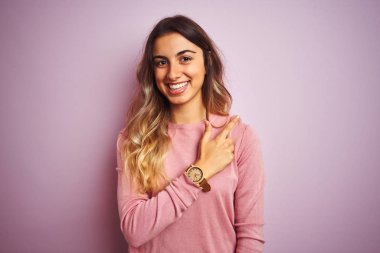 Genç güzel kadın pembe izole arka plan neşeli üzerinde bir kazak giyen yüzünde mutlu ve doğal ifade ile yan yana el ve parmak ile işaret eden yüz bir gülümseme ile neşeli