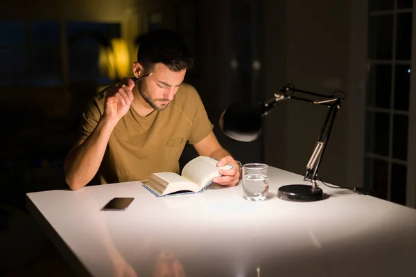 Young handsome man studying at home, reading a book at night — Stock Photo, Image