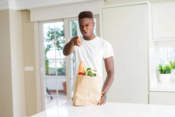 African american man holding paper bag full of fresh groceries pointing with finger to the camera and to you, hand sign, positive and confident gesture from the front