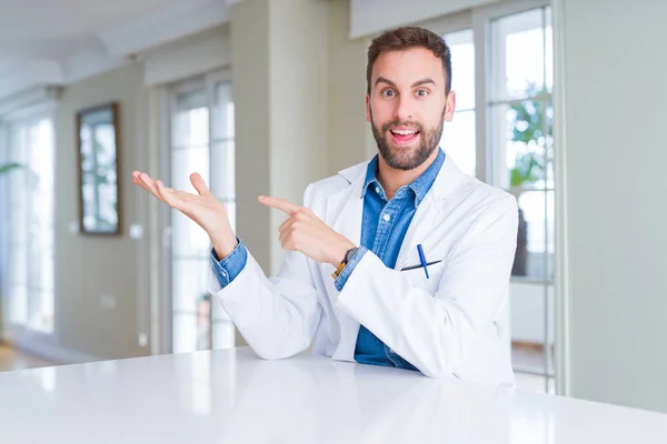 Przystojny Lekarz Mężczyzna Noszenie Płaszcz Medyczny Klinice Zdumiony Uśmiechnięty Aparatu — Zdjęcie stockowe