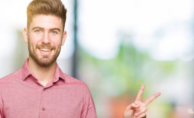 Mutlu yüz zafer işareti yaparken kameraya göz kırpıyor ile gülümseyen genç yakışıklı iş casual adam. İki numaralı.