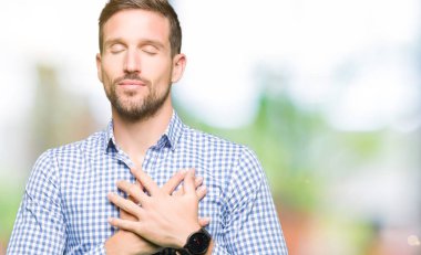 Göğüs kapalı gözler ve yüzünde minnettar jest ile gülümseyen mavi gözlü yakışıklı iş adamı eller. Sağlık kavramı.