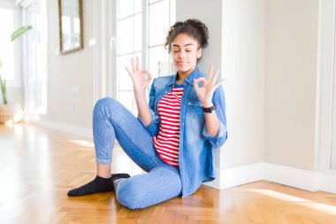 Afro saçlı güzel genç Afrikalı Amerikalı kadın yerde oturan Relax ve gözleri ile gülümseyen meditasyon jest parmaklar ile kapalı. Yoga konsepti.