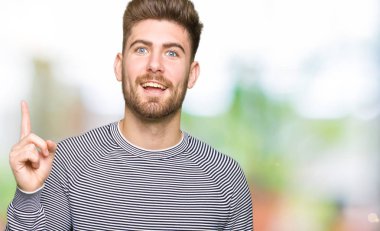 Çizgi kazak giyen genç yakışıklı adam başarılı bir fikir ile parmak yukarı işaret. Çıkıldı ve mutlu. Bir numara.