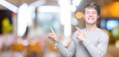 Gülümseyen ve iki elleri ve parmakları ile tarafına işaret kamera bakarak izole arka plan üzerinde kış kazak giyen genç yakışıklı adam.