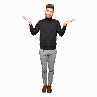 Genç yakışıklı sarışın adam kış kazak clueless ve kollar ve elleri ile karıştı ifade giyiyor kaldırdı. Şüphe kavramı.