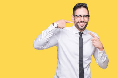 Kendinden emin gösterilen ve işaret parmakları diş ve ağız ile gülümseyen izole arka plan üzerinde gözlük takan genç yakışıklı iş adamı. Sağlık kavramı.