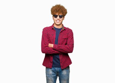 Kameraya bakarak çapraz silah ile gülümseyen güneş gözlüğü mutlu yüz giyen afro saçlı Genç yakışıklı adam. Olumlu bir kişi.