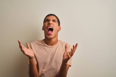 Genç yakışıklı Arap adam izole beyaz arka plan üzerinde çizgili t-shirt giyen deli ve deli bağırarak ve agresif ifade ve kollar kaldırdı ile bağırıyor. Hayal kırıklığı kavramı.