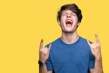 Genç yakışıklı adam el yukarı ile kaya sembolü yapıyor çılgın ifade ile bağırarak izole arka plan üzerinde mavi t-shirt giyiyor. Müzik yıldızı. Ağır kavram.